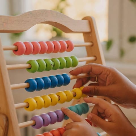 Close-up of an adult's hands and a child's hands counting colorful beads on a wooden learning frame